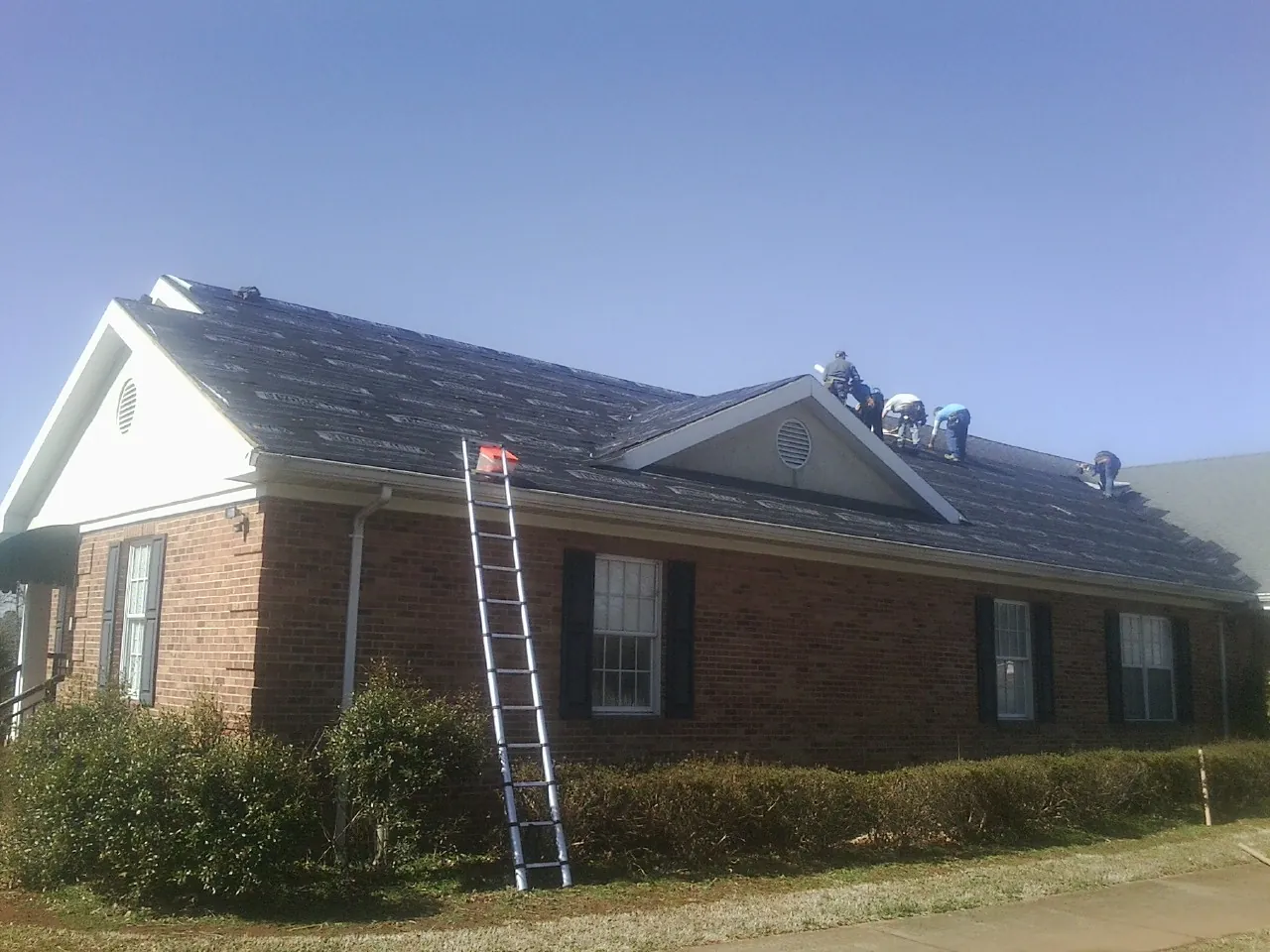 Crew tearing shingles off a brick ranch roof with a ladder set — Emergency Roof Repair work by our crew in Spring Green