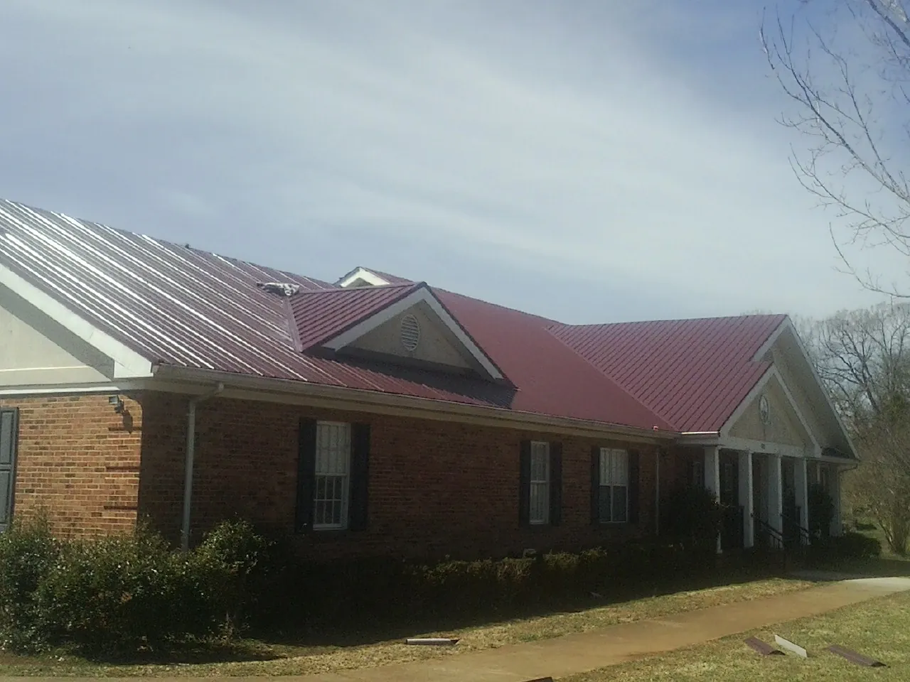 Red metal roof with gabled entries on a long brick building, from a Hail Damage Roof Repair job in Spring Green