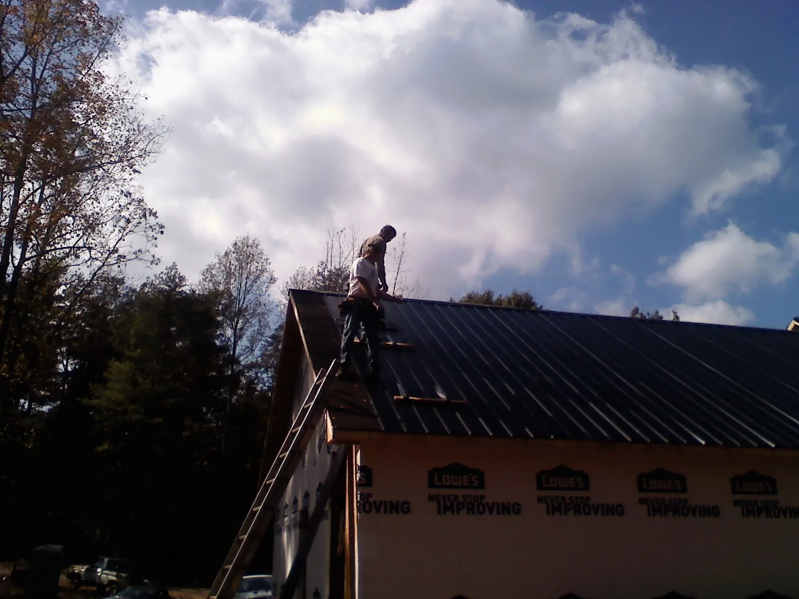 Roofer fastening dark metal panels high against a cloudy sky, from a Roof Inspection job in Spring Green